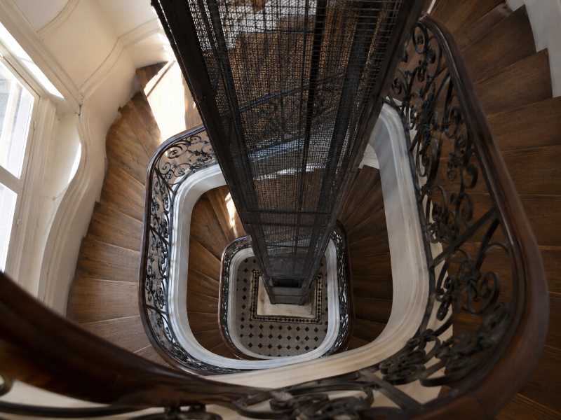 Cage d’escalier ancienne avec une cabine d’ascenseur étroite dans un immeuble parisien